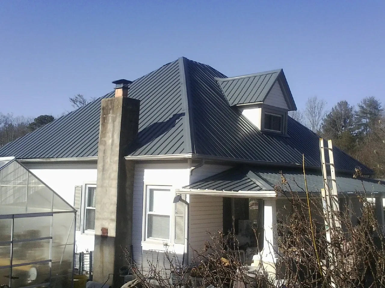 Dark blue standing seam metal roof on a white farmhouse with dormer — Slate & Tile Roof Repair by Roofing Brothers in Glencoe