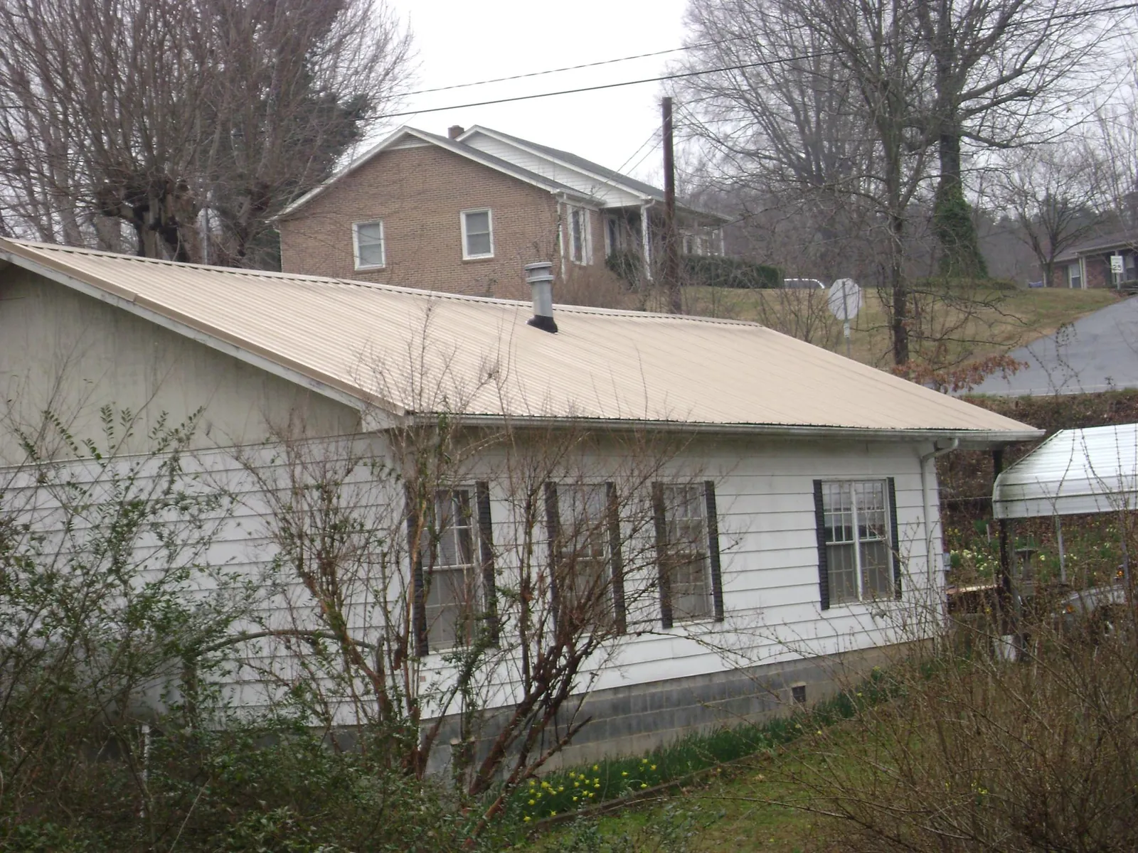 Tan metal roof on a white sided house set into a hillside — Commercial Roofing by Roofing Brothers in Glencoe